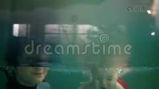 妈妈和她的宝宝穿着可爱的红色短裤在室内游泳池里玩得很开心。 一起潜水视频