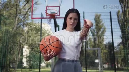 漂亮的黑发女人，带着一个篮球球，挑战观众，她的手指指向相机。 体育概念视频