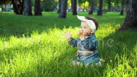 可爱的小女孩穿着牛仔裤，发带坐在阳光明媚的公园里绿草如茵视频