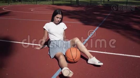 可爱的黑发少女，带着篮球，看着坐在户外篮球场上的摄像机视频