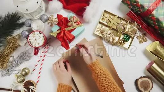 女性手在木桌上写礼物清单，有礼物、包装纸、红色圣诞装饰品。视频