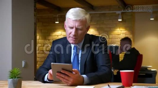 一个老白种人商人在平板电脑上浏览，在办公室的室内喝咖啡的特写镜头视频