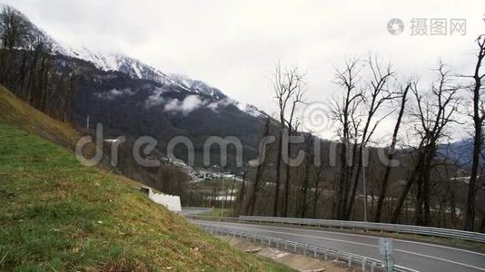 一条山路和一辆移动的汽车在多云的背景下与雪山的呼吸景观。 库存数据视频