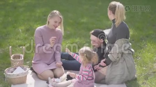 两个母亲和他们的孩子在公园的毯子上。 一个金发大男孩躺在毯子上，一个可爱的小女孩在里面视频