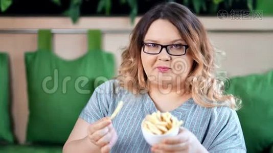 快乐胖女人吃着开胃的炸薯条摆姿势看镜头的画像视频