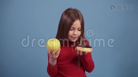 可爱的小女孩选择了一个巧克力圈，上面覆盖着五颜六色的喷头和一个绿色的新鲜苹果，决定。视频