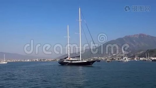 美丽的大游艇停泊在蓝色平静的大海上，背景是美丽的小山和船在一个视频