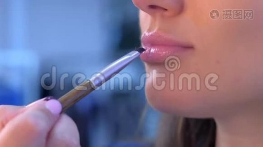 化妆师将唇彩用刷子涂在女孩模特的嘴唇上化妆。视频