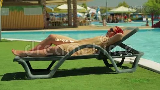 一位穿着浴袍的年轻女子在游泳池附近的一张躺椅上晒太阳。视频