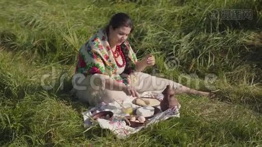 美丽的超重女人坐在草地上，准备吃带有干酪和蜂蜜的煎饼。 健康视频