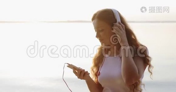 肖像红头雀斑的女孩戴着白色耳机正在听歌和微笑。视频