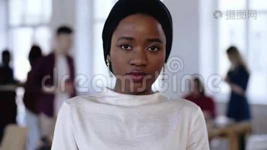 穿着民族头巾的年轻严肃的非洲企业经理女士看着镜头，在时髦的阁楼办公室微笑。视频
