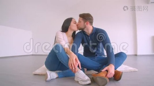 在白墙背景下，一对正在进行的白种人夫妇坐在新的空平拥抱和亲吻的地板上快乐着视频