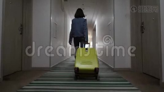 一个年轻的女孩带着一个手提箱沿着酒店走廊走。 入住酒店.. 从后面看。 4k决议视频