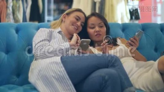 快乐的购物女性使用智能手机，坐在购物中心大笑视频