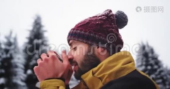一个人在寒冷的冬天在雪林中喝热茶的肖像，他欣赏周围的风景视频