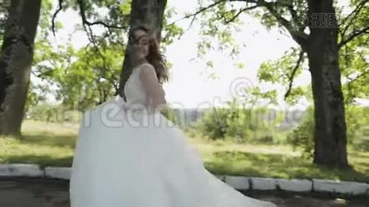美丽可爱的新娘穿着婚纱在公园里奔跑。 慢动作视频