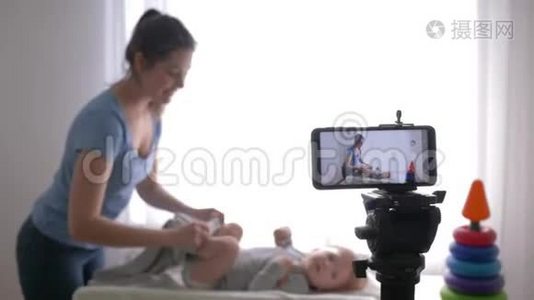 工作博客作者、年轻妈妈vlogger在智能手机上录制教育视频时，给蹒跚学步的男孩换衣服视频