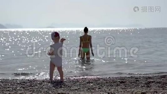 一个小男孩在海里扔一颗鹅卵石，女孩在海里游泳，慢动作视频