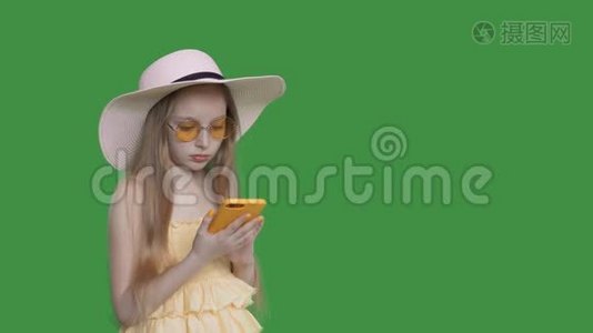穿黄色连衣裙和太阳镜的年轻女孩在透明的绿色背景上使用手机。 夏天的少女视频