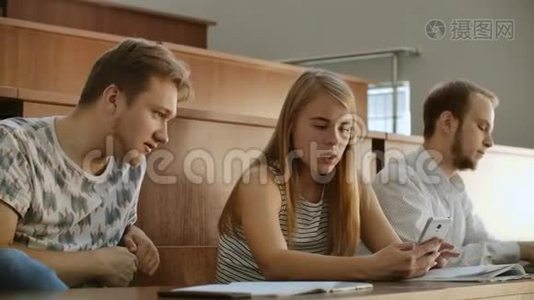 漂亮的女学生正在使用智能手机，看屏幕，有说有笑，坐在大学的桌子上。 社会视频