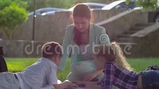 在户外看书，快乐的女家庭教师为小男孩和小女孩在阳光明媚的露天草地上坐着看书视频