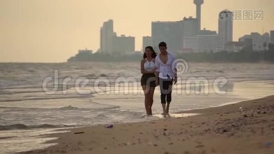 年轻的男女赤着脚携手走在沙滩上慢动作的女孩和她的男朋友在一起视频