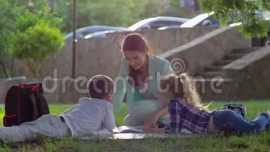 开朗的女教育家为小男孩和小女孩在阳光明媚的阳光下坐在大自然的绿草上读书视频