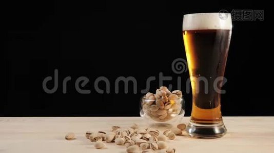 新鲜啤酒。 在黑色背景下，手工从靠近开心果碟的木桌上拿出一杯美味的手工啤酒视频