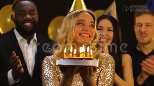 戴着生日帽的金发女人微笑着在蛋糕上吹蜡烛，朋友们鼓掌视频