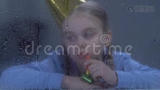 悲伤孤独的女孩，带着派对鼓风机在雨中看着窗户，没有朋友视频