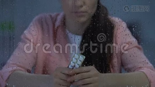 抑郁孤独的女性在雨窗附近拿着一包水泡药丸，疾病视频