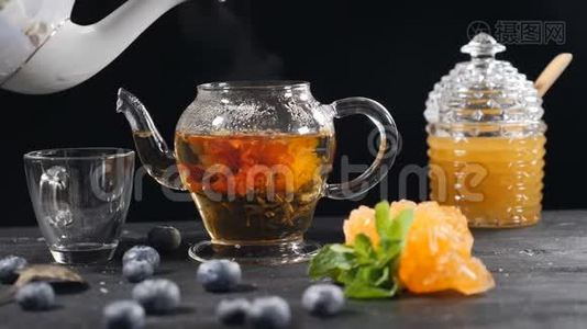 在玻璃茶壶里倒开水。 绿色的中国花茶绽放。 红花茶的漂浮。 蓝莓视频