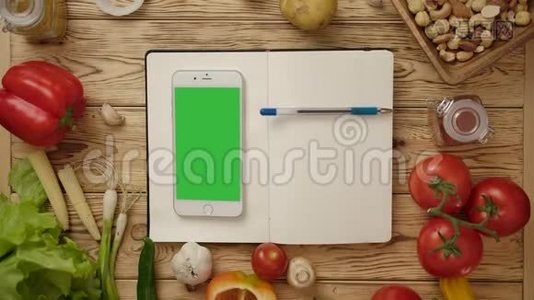 笔在空白笔记本上滚动，智能手机在厨房桌上放蔬菜视频