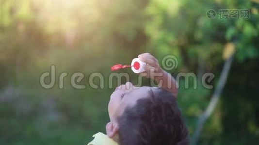 小男孩在大自然的绿色背景下吹肥皂泡视频