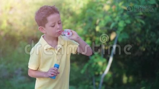 小男孩在大自然的绿色背景下吹肥皂泡视频