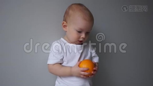 这孩子手里拿着一个橘子，一个两岁蓝眼睛男孩的肖像。 健康饮食视频