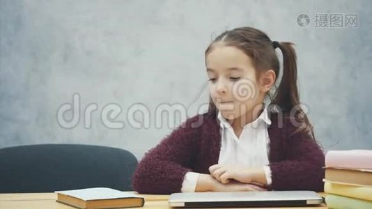一个女学生坐在桌子旁。 在此期间，选择一本书或笔记本电脑。 在灰色背景下快乐。视频