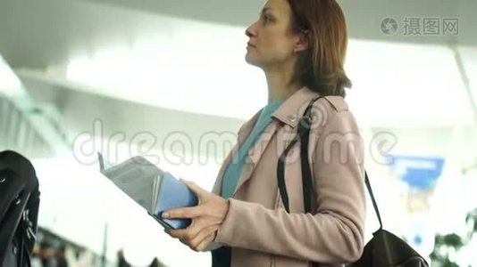 机场的一位棕色头发的女人看着航班时间表。 她手里拿着护照和机票视频