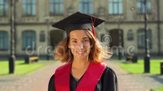 戴着黑色斗篷和帽子的自信可爱女孩站在大学大楼前看镜头的肖像视频