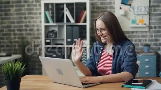 办公室里一个快乐的女人看着笔记本电脑屏幕边说话边挥手视频