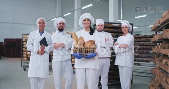 微笑，魅力年轻的贝克女士和所有主要的面包师团队在面包店制造的中间，直视。视频