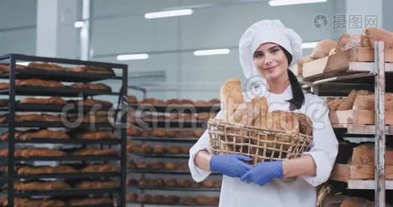 面包行业的年轻女性面包师拿着一篮子新鲜的烘焙面包，直视着相机，笑得很漂亮视频