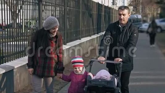 家庭步行在公园步行与婴儿车与一个幼儿和一个3-4岁的孩子。 家庭观念。 户外活动视频