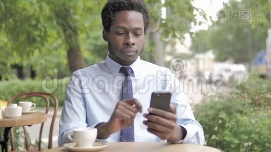 非洲商人坐在户外咖啡厅，在智能手机上失声喧哗视频