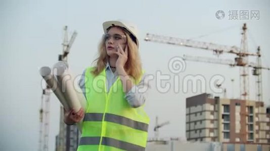 一位戴着头盔的女工程师在建筑背景下与起重机通话的肖像视频
