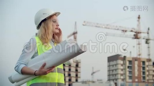 会说话的女人戴着头盔在电话里，背景是施工，手里拿着起重机图纸。 女性视频