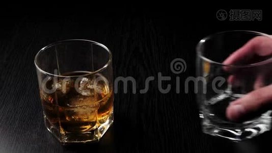豪华威士忌。 手把空杯子放在玻璃旁边，在黑桌上放着真正冷冰的金色威士忌。 不倒翁威士忌。视频