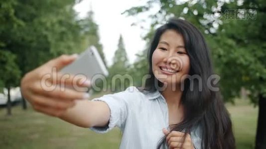 美丽的亚洲女孩用智能手机相机在户外自拍的慢动作视频