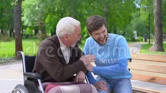坐在轮椅上的老年男性和志愿者一起欢笑和开玩笑，一起玩视频